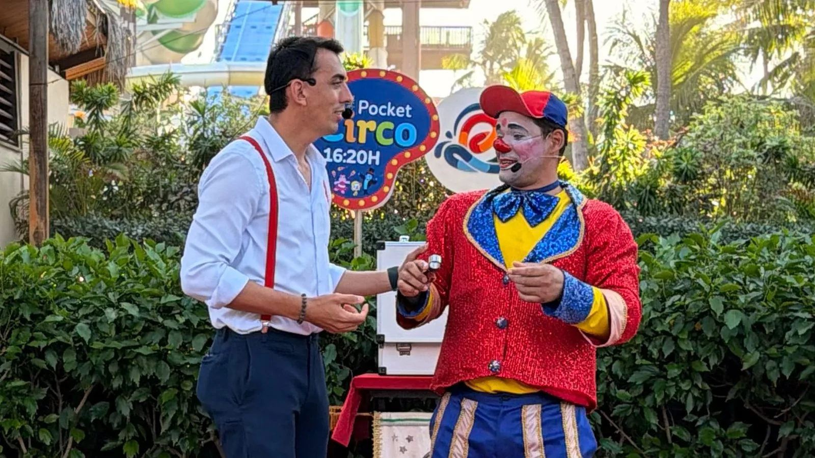 Grupo Palhamágicos em cena: palhaço de casaco vermelho e mágico de suspensórios apresentam-se ao ar livre, diante de uma placa de “Pocket Circo”.