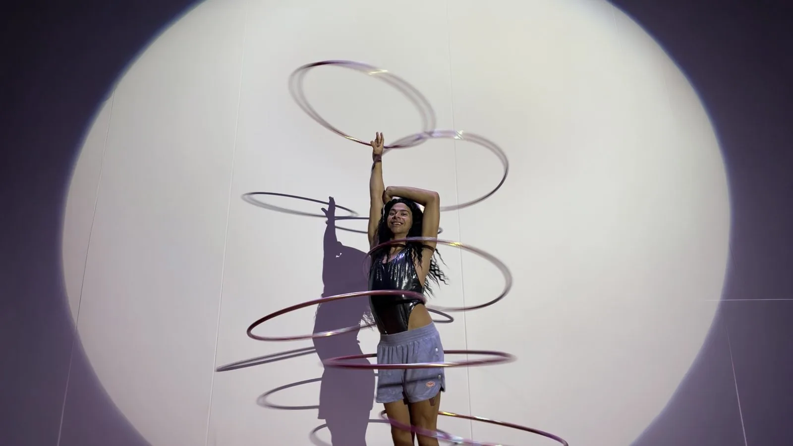 Vicky Roman em cena: a artista gira bambolês que desenham círculos de luz lilás dentro de uma lona branca.